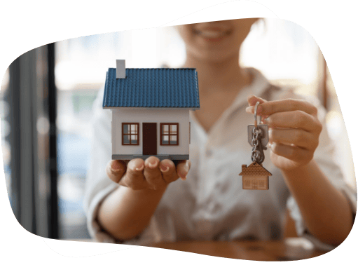 Mulher segurando e mostrando uma chave e uma casa miniatura nas mãos